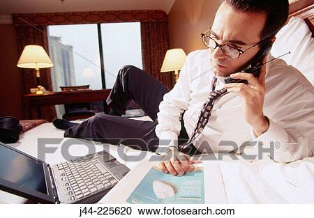Businessman talking on cell phone on the bed in a hotel room View Large Photo Image Stock Image - Businessman talking on cell phone on the bed in a hotel room. Fotosearch