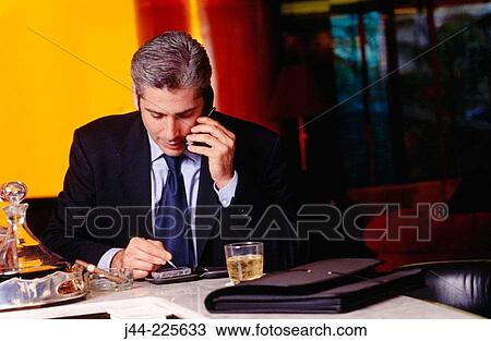 Businessman talking on cell phone while using palm pilot in a bar View Large Photo Image Stock Image - Businessman talking on cell phone while using palm pilot in a bar. Fotosearch