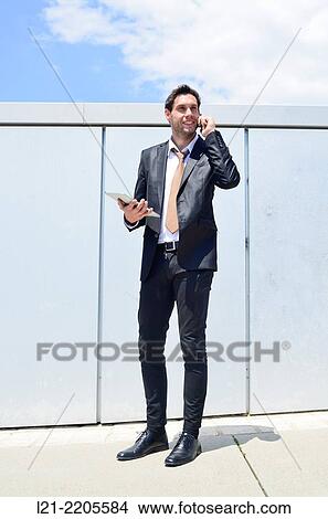 Businessman talking on mobile while carrying a tablet. View Large Photo Image Picture - Businessman talking on mobile while carrying a tablet.. Fotosearch