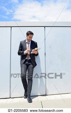 Businessman using a tablet, standing, leaning on a wall. View Large Photo Image Stock Image - Businessman using a tablet, standing, leaning on a wall.. Fotosearch
