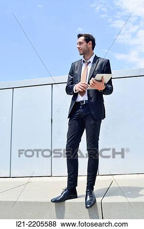 Businessman using a tablet, standing, near a wall outdoors. View Large Photo Image Stock Photo - Businessman using a tablet, standing, near a wall outdoors.. Fotosearch