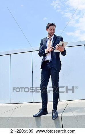 Businessman using a tablet, standing, near a wall outdoors. View Large Photo Image Stock Photo - Businessman using a tablet, standing, near a wall outdoors.. Fotosearch