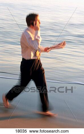 Stock Photography - Businessman walking quickly on the beach. Fotosearch