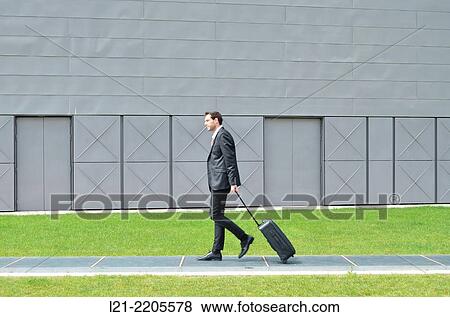 Stock Photo - Businessman walking with a suitcase on wheels.. Fotosearch
