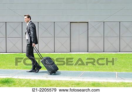 Stock Photo - Businessman walking with a suitcase on wheels.. Fotosearch