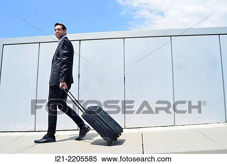 Businessman walking with a wheeled down a hallway in front of a wall outdoors. View Large Photo Image Stock Photography - Businessman walking with a wheeled down a hallway in front of a wall outdoors.. Fotosearch
