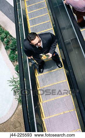 Stock Image - Businessman with flowers in hand on scalator. Fotosearch