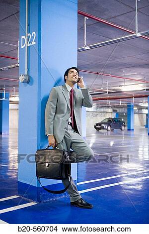 Picture - Businessman with mobile phone. Parking lot.. Fotosearch