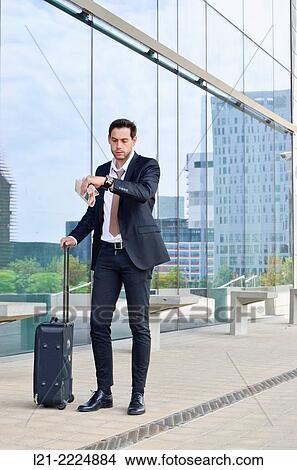 Businessman with wheeled suitcase looking at wrist watch. View Large Photo Image Picture - Businessman with wheeled suitcase looking at wrist watch.. Fotosearch