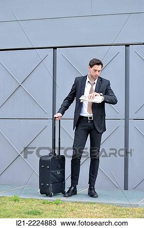 Businessman with wheeled suitcase looking at wrist watch. View Large Photo Image Stock Image - Businessman with wheeled suitcase looking at wrist watch.. Fotosearch