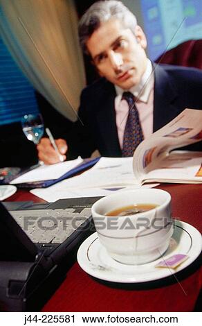 Businessman working on a desk with a cup of tea in the office View Large Photo Image Stock Image - Businessman working on a desk with a cup of tea in the office. Fotosearch