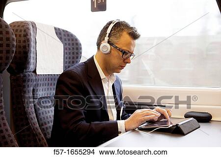 Businessman working on a tablet on a commuter train View Large Photo Image Picture - Businessman working on a tablet on a commuter train. Fotosearch