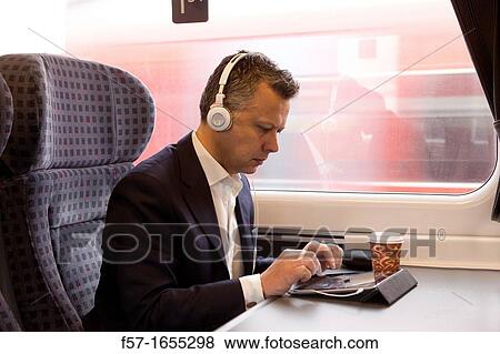 Businessman working on a tablet on a commuter train View Large Photo Image Stock Photo - Businessman working on a tablet on a commuter train. Fotosearch