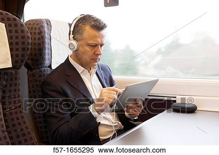 Stock Photography - Businessman working on a tablet on a commuter train. Fotosearch