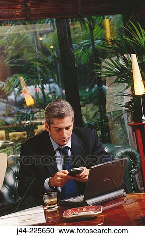 Businessman working with laptop computer and palm pilot in a hotel lounge View Large Photo Image Stock Image - Businessman working with laptop computer and palm pilot in a hotel lounge. Fotosearch