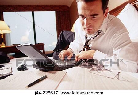 Businessman working with laptop computer on the bed in a hotel room View Large Photo Image Stock Photo - Businessman working with laptop computer on the bed in a hotel room. Fotosearch