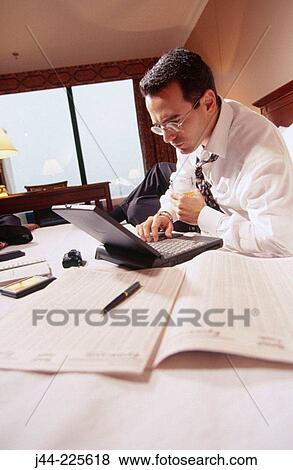 Businessman working with laptop computer on the bed in a hotel room View Large Photo Image Stock Photo - Businessman working with laptop computer on the bed in a hotel room. Fotosearch