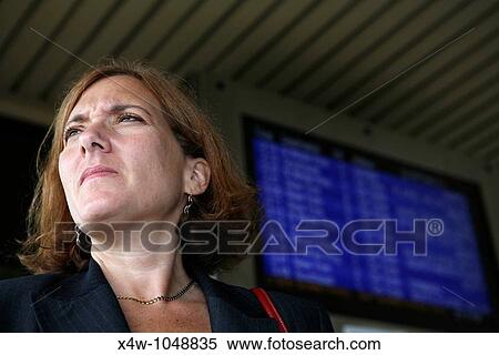 Stock Photography - Businesswoman awaits her commuter train standing near platform timetable. Fotosearch