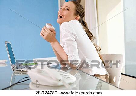 Stock Image - businesswoman by laptop holding cup, portrait. Fotosearch