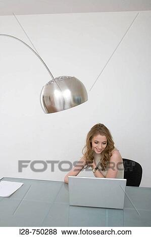 Businesswoman sitting at a table and working on a laptop View Large Photo Image Stock Photo - Businesswoman sitting at a table and working on a laptop. Fotosearch