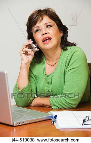 Businesswoman sitting on desk with laptop computer and talking on the phone in an office View Large Photo Image Stock Photo - Businesswoman sitting on desk with laptop computer and talking on the phone in an office. Fotosearch