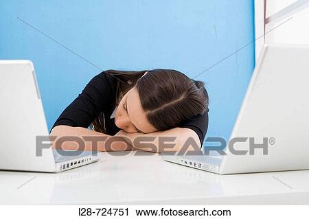 Stock Image - Businesswoman sleeping on desk in front of laptops. Fotosearch