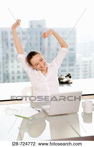 Stock Image - Businesswoman stretching at desk. Fotosearch