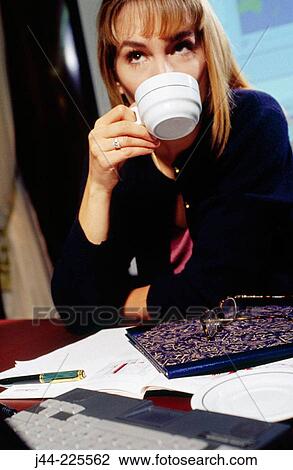 Businesswoman working on a desk with a cup of coffee in an office View Large Photo Image Stock Image - Businesswoman working on a desk with a cup of coffee in an office. Fotosearch