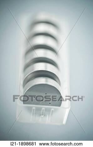 Stock Image - Button cells in row within a transparent plastic container. Batteries ready for recycling.. Fotosearch