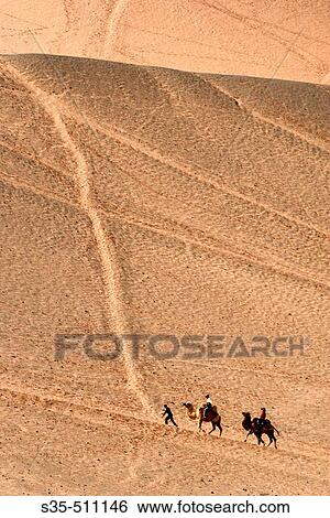 Stock Photograph - Camels carry passengers in the desert, Turpan, Xinjiang Province, China. Fotosearch
