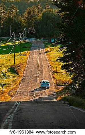 Car driving on a bumpy, asphalt, rural road in Lancaster, NH at the end of the day. View Large Photo Image Picture - Car driving on a bumpy, asphalt, rural road in Lancaster, NH at the end of the day.. Fotosearch