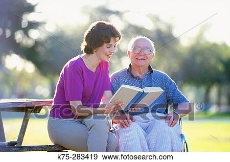 Stock Photo - Caretaker reading to senior in the park. Fotosearch