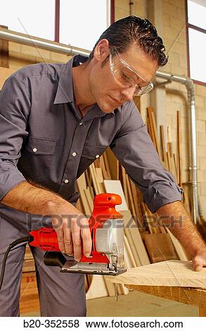 Stock Photo - Carpenter cutting wood plank with fretsaw. Fotosearch
