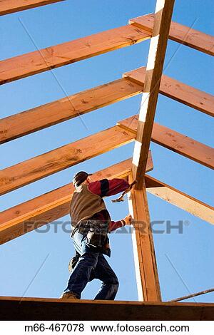 Carpenter hammering a nail into a center post while framing a roof at a construction site. View Large Photo Image Stock Photo - Carpenter hammering a nail into a center post while framing a roof at a construction site.. Fotosearch