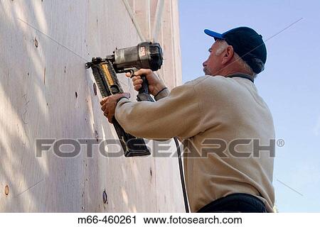 Carpenter shooting nails into plywood siding of a building under construction. View Large Photo Image Stock Image - Carpenter shooting nails into plywood siding of a building under construction.. Fotosearch