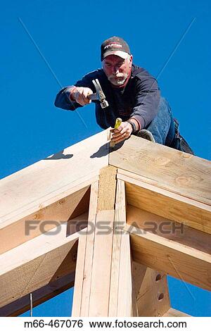 Carpenter standing at the edge of a framed roof, reaching over to cut a notch into the peak of the wall at a construction site. View Large Photo Image Stock Photograph - Carpenter standing at the edge of a framed roof, reaching over to cut a notch into the peak of the wall at a construction site.. Fotosearch