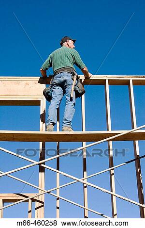 Carpenter standing on scaffolding looking over the top of second story wall at a construction site. View Large Photo Image Stock Photo - Carpenter standing on scaffolding looking over the top of second story wall at a construction site.. Fotosearch