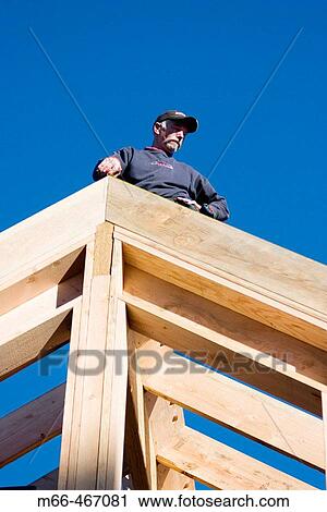 Carpenter standing on the peak of a framed in roof, looking down the rafters at a construction site. View Large Photo Image Stock Image - Carpenter standing on the peak of a framed in roof, looking down the rafters at a construction site.. Fotosearch