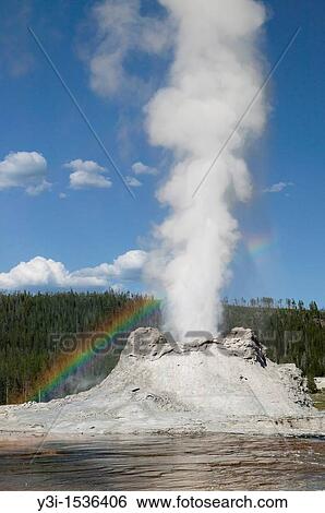 Stock Photograph - Castle Geyser erupting with a rainbow in its mist in Yellowstone National Park, Wyoming, USA. Fotosearch