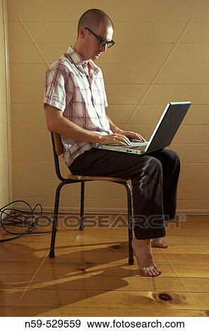 Stock Photo - Casual young man working on laptop in empty room.. Fotosearch
