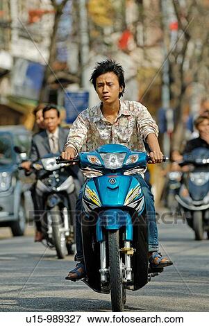 Stock Photo - Casually dressed young Vietnamese man riding on a small motorbike through the old quarter of Hanoi, Vietnam. Fotosearch