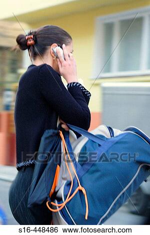 Casually dressed young woman speaking on the cell phone while holding heavy luggage View Large Photo Image Stock Photograph - Casually dressed young woman speaking on the cell phone while holding heavy luggage. Fotosearch