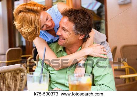 Stock Image - Caucasian couple at outdoor cafe hugging and laughing. Fotosearch