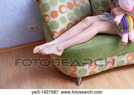 Stock Photo - Caucasian female bare legs indoors on sofa. Fotosearch