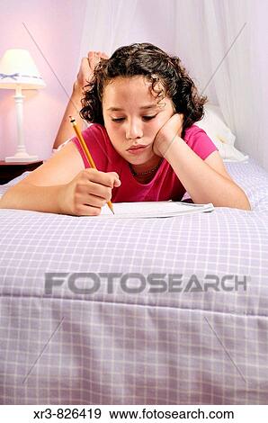 Stock Photo - Caucasian female child laying on bed in pink bedroom working on homework. Fotosearch