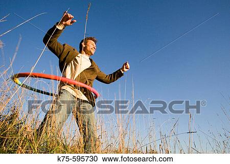 Stock Image - Caucasian male, age 30's to 40? s, hula hoop, outdoors, field, blue sky, happy, joyful. Fotosearch