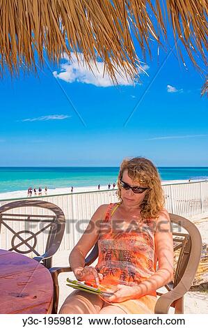 Caucasian woman, 45, using digital tablet device on a beach in Florida, USA. View Large Photo Image Stock Image - Caucasian woman, 45, using digital tablet device on a beach in Florida, USA.. Fotosearch
