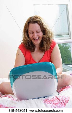 Caucasian woman in her 20's reading email laughing on bed in her bedroom. View Large Photo Image Stock Image - Caucasian woman in her 20's reading email laughing on bed in her bedroom.. Fotosearch