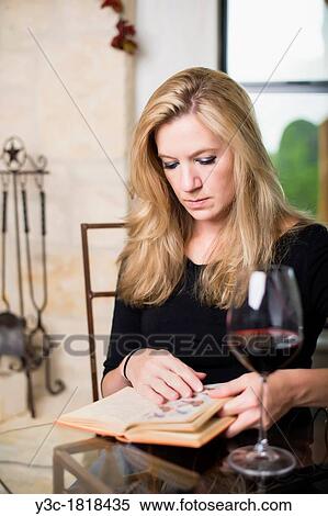 Stock Photography - Caucasian woman in her 30s reading a book while having a glass of red wine. Fotosearch