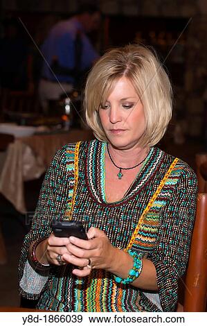Caucasian woman in her 40s reading or writing a text message on her smartphone while sitting at a restaurant table View Large Photo Image Stock Photo - Caucasian woman in her 40s reading or writing a text message on her smartphone while sitting at a restaurant table. Fotosearch